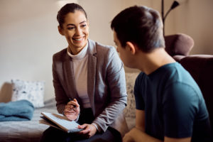 Happy psychologist talking to man with down syndrome while visiting him at home.